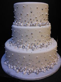 a three tiered white wedding cake with pearls