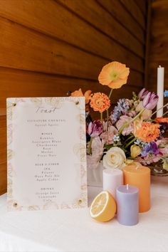 an arrangement of flowers and candles on a table with a menu in front of it