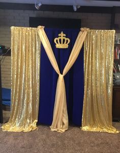 gold sequin drapes with a crown on top and blue curtains behind them in front of a brick wall