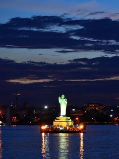 the statue of liberty is lit up at night in front of a city skyline and water