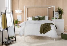 a white bed sitting in a bedroom next to a tall mirror and plant on the wall