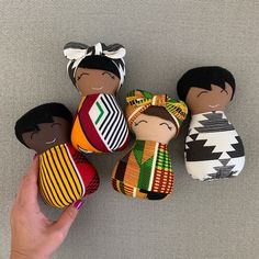 a hand is holding five small dolls in different colors and patterns, each with an individual's finger