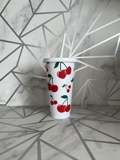 a white cup with cherries on it sitting on a marble floor next to a wall