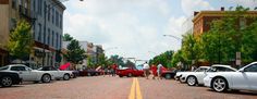 several cars parked on the side of a road with people walking down it and buildings in the background