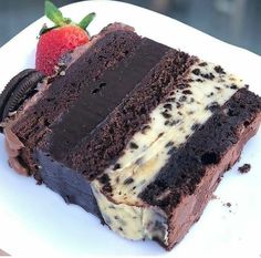 a piece of chocolate cake with oreo cookies and strawberries on the side, sitting on a white plate