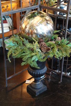 a vase filled with pine cones and greenery on top of a wooden table next to a metal rack