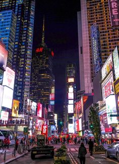 a busy city street at night with lots of neon signs and people walking on the sidewalk