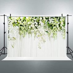 a white backdrop with flowers and greenery hanging from the wall in front of it