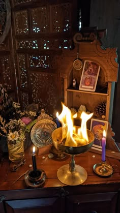 a table topped with a bowl filled with fire next to candles and pictures on top of it