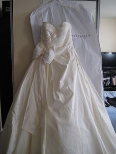 a white wedding dress hanging on a hanger next to a bed with a pillow