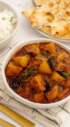 some food is in a white bowl on a table next to rice and pita bread