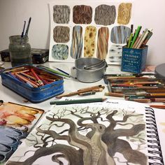 a table topped with lots of art supplies next to a container of paint and pencils