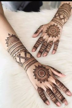 two hands with henna tattoos on them sitting on top of a white furnish