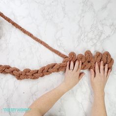 someone crocheting a piece of rope on top of a marble surface with their hands