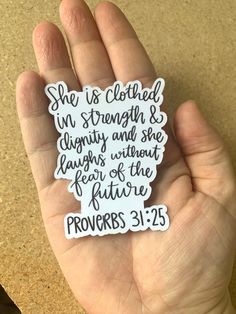 a hand holding a sticker that says she is clothed in strength and she laughs without fear of the future proves 31 25