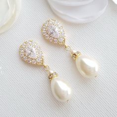 two pairs of pearl and crystal earrings on top of a white cloth with flowers in the background