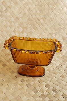 a yellow glass dish sitting on top of a wooden stand next to a woven wall