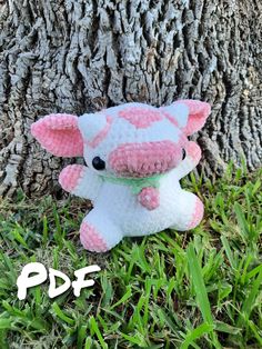 a pink and white stuffed cow sitting next to a tree