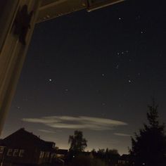 the night sky is lit up with stars and clouds in the distance as seen from an open window