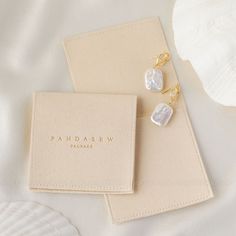 two pairs of pearl earrings sitting on top of a white book next to a seashell