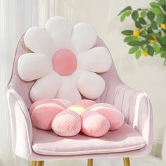 a pink chair with white flowers on the back and four pillows in front of it