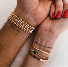 two people holding hands with tattoos on their wrists and wristbands, both wearing matching bracelets