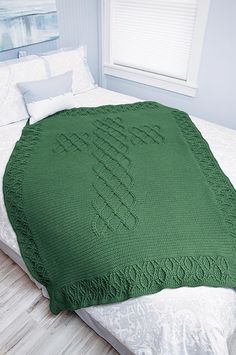 a large green blanket on top of a bed in a room with white walls and wood flooring