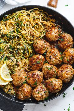 meatballs and noodles are in a skillet with lemon wedges on the side