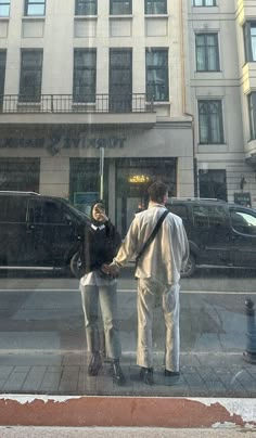 a man and woman are standing in front of a building on the street holding hands