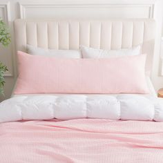 a bed with pink and white sheets, pillows and a plant in a vase on the headboard