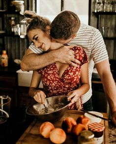 a man hugging a woman in the kitchen while she is mixing something into a bowl