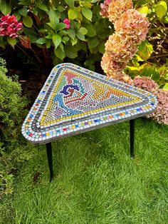 a mosaic table sitting in the grass next to flowers