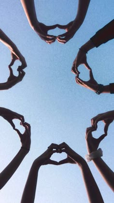 four hands making a heart shape with their fingers in the air against a blue sky