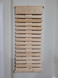 a wooden slatted wall hanging on the side of a white wall next to a door