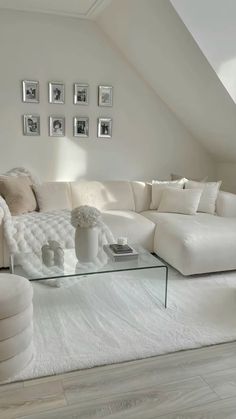 a living room with white couches and pictures on the wall above them, along with a glass coffee table