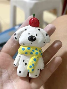 a hand holding a small toy dog with a cherry on it's head