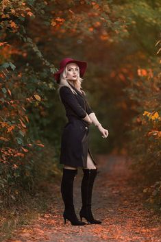 a woman in black dress and red hat posing for the camera on a path surrounded by trees