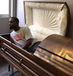 a man sitting in a wooden casket next to a window with white sheets on it