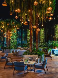 an outdoor restaurant with lots of plants and lights hanging from the ceiling, along with wooden flooring