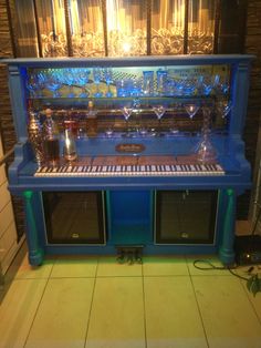 a blue piano sitting on top of a tiled floor next to a wall filled with glass bottles