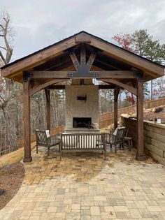 a covered patio with two benches and a fire place in the middle, surrounded by brick pavers