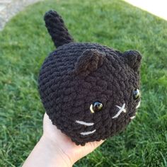 a hand holding a black crocheted cat hat on top of the green grass