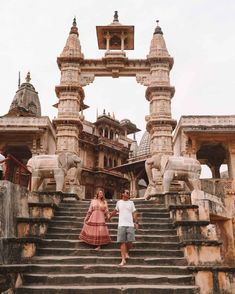 a man and woman walking up some steps in front of an old building with statues on it