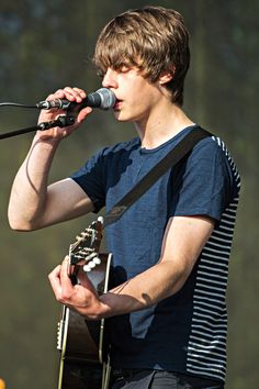 a young man holding a guitar and singing into a microphone