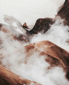 two people standing on top of a mountain surrounded by clouds