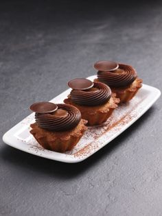 three cupcakes on a white plate topped with chocolate