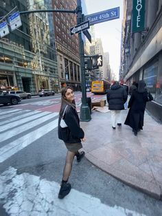 a woman standing on the side of a road next to a street sign and buildings