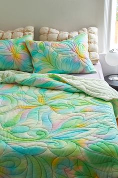 a bed covered in a colorful comforter next to a window with white pillows on it