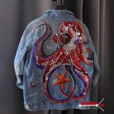 a denim jacket with an octopus on it hanging from a clothes rack in front of a curtain