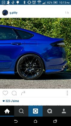 a blue car parked in front of a green bush on the side of the road